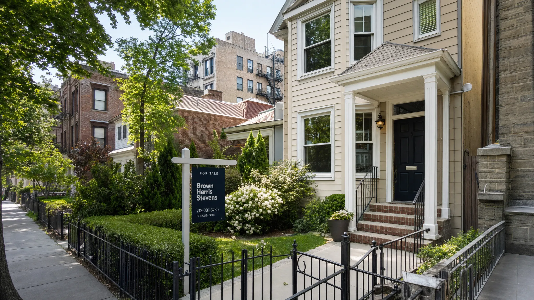 A New York residential street with a mix of townhomes, apartment buildings, and single-family homes, showing a real estate sign in front of a well-presented property from a slightly elevated corner view.